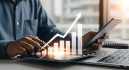 Businessman reviewing a rising financial growth chart on a tablet while working on a laptop, symbolizing business success and progress