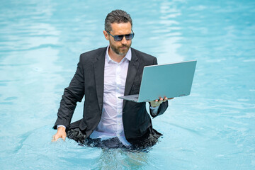 Crazy Business man in suit wit laptop in swimming pool. Crazy summer freelancer working in pool....