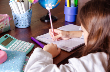 A young girl doing her maths homework with school supplies on a wooden table. 
