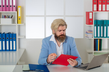 Serious auditor inspector working with clipboard paper files and laptop. Searching business...