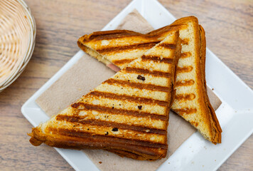 Crispy toasted Spanish bikini sandwich filled with ham slice and melted cheese, presented on...