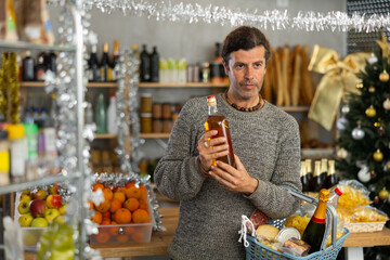 Middle-aged man with contemplative expression examining bottle of whiskey in warmly decorated...