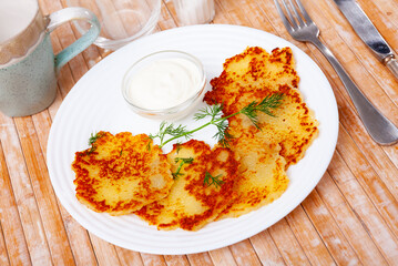 Appetizing potato pancakes served with sour cream on platter