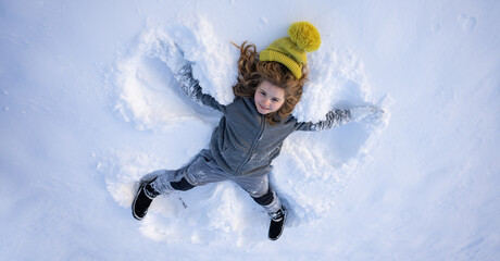 Funny child and snow in the park. Kid plays joyfully in snowfall. Winter kids portrait. Snowflakes...