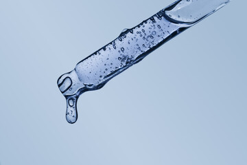 Cosmetic serum dropper with drop hanging in the air transparent texture on blue background