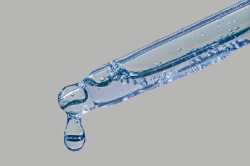 Cosmetic serum dropper with drop hanging in the air transparent texture on grey background