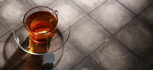 Cup of hot tea on grey tile background with space for text