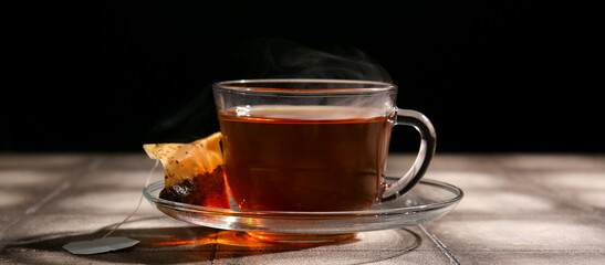 Cup of hot tea on table against dark background, closeup