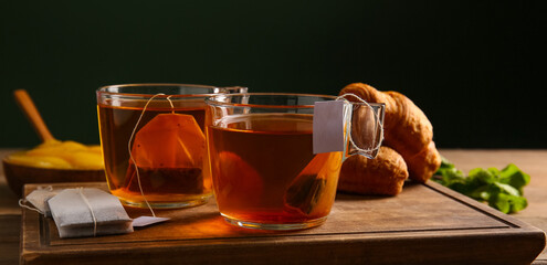 Cups of hot tea and croissants on table against dark background
