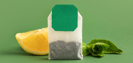 Tea bag, lemon slice and mint leaves on green background, closeup