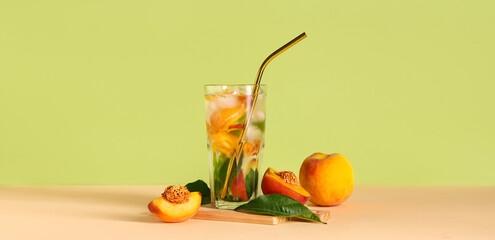 Glass of tasty peach lemonade on table against green background