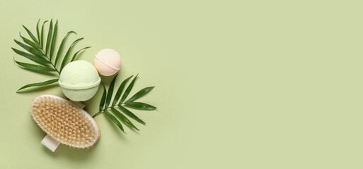 Bath bombs, massage brush and tropical leaves on green background with space for text, top view