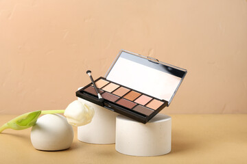 Plaster podiums with palette of eyeshadows, brush and tulip flower on beige background