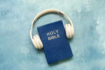 Holy Bible with headphones on blue background