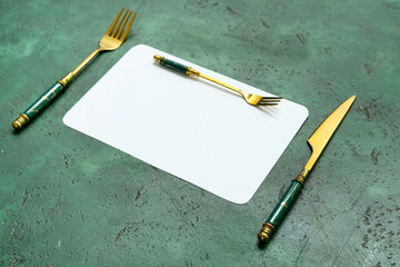 Blank card and stainless steel cutlery on green background, closeup