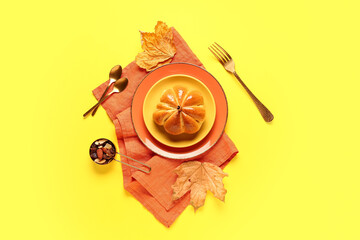 Plates with tasty pumpkin shaped bun on yellow background