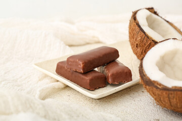 Plate with tasty chocolate covered coconut candies on light background