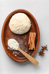 Plate with raw dough, flour and spices for preparing bakery on light background
