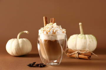 Glass of tasty pumpkin latte with cinnamon and almond on brown background