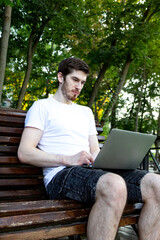 Casual man sitting in park with laptop. Typing and working remotely outside. concept of remote work, flexibility, and digital freedom in a natural environment