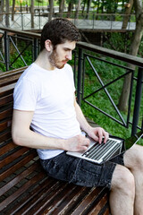 Man working on laptop in summer park. Green trees in background, peaceful atmosphere.