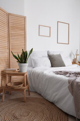 Interior of light bedroom with big bed, frames and stool