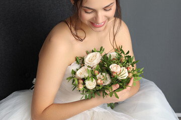 Beautiful young bride in wedding dress with bouquet sitting on dark background, closeup