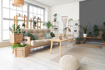 Stylish interior of living room with comfortable sofa, table, houseplants, shelving units and window
