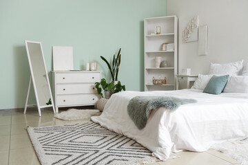 Stylish interior of modern bedroom with comfortable bed, shelving unit and white chest of drawers
