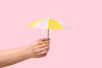 Female hand with mini umbrella on pink background