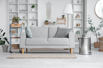 Interior of light living room with sofa, shelf units and trash bin