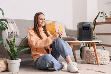 Young woman using mobile phone and portable power station at home