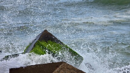 Rocky breakwater extending into the Caribbean Sea. Waves are crashing against the rocks, creating white spray and foam. 