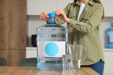 Woman opening bottle of clean water on table in kitchen