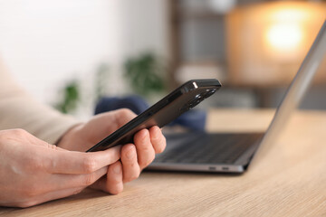 Woman using modern smartphone at wooden table indoors, closeup