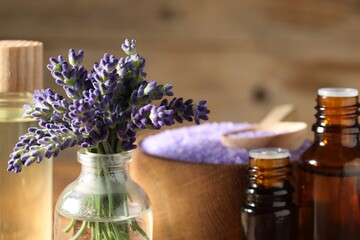 Bottles of lavender essential oil, sea salt and flowers on table, closeup