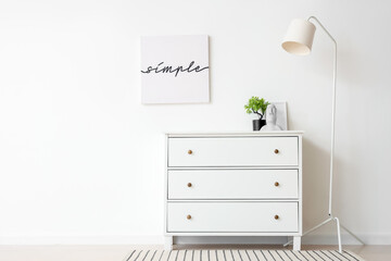 Interior of light room with commode, lamp and poster
