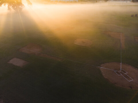 Baseball diamonds are shimmering under golden sunlight and morning mist in open sports complex - Powered by Adobe