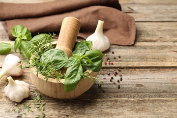 Mortar with pestle, different aromatic herbs and spices on wooden table, space for text