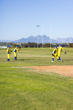 Male baseball teammates practicing catching fly ball on grass outfield near white rugby goalposts