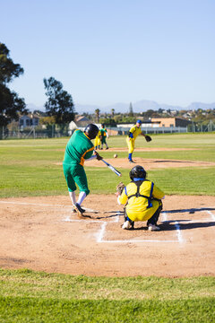 Diverse male athletes swinging metal bat, catching baseball near chalk baselines on community field