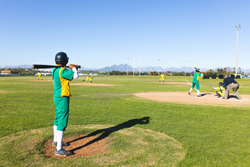 Man in green and yellow uniform standing in on-deck circle gripping bat on grass, copy space