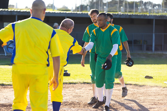 Diverse male baseball players shaking hands on infield dirt near dugout with helmets and cleats