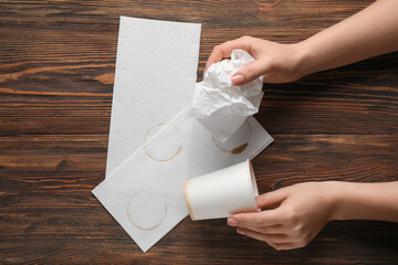 Female hand with paper cup, napkins and coffee stains on wooden background