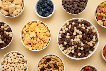 Bowls with different tasty cereals and berries on beige background