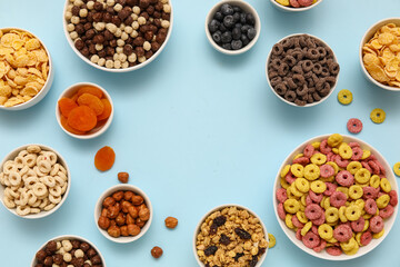 Frame made of bowls with different tasty cereals, berries, dry fruits and nuts on blue background