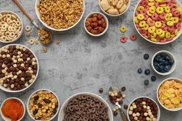 Frame made of bowls with different tasty cereals, berries, dry fruits and nuts on grunge grey...