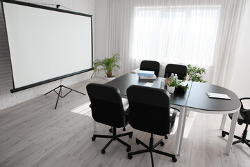 Interior of conference hall with table, houseplants and projector screen in modern office