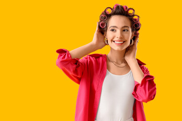 Young woman with hair curlers on yellow background
