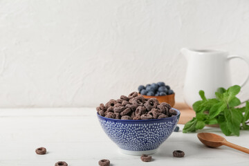 Bowl of chocolate cereal rings with spoon, mint leaves and blueberries on white wooden table
